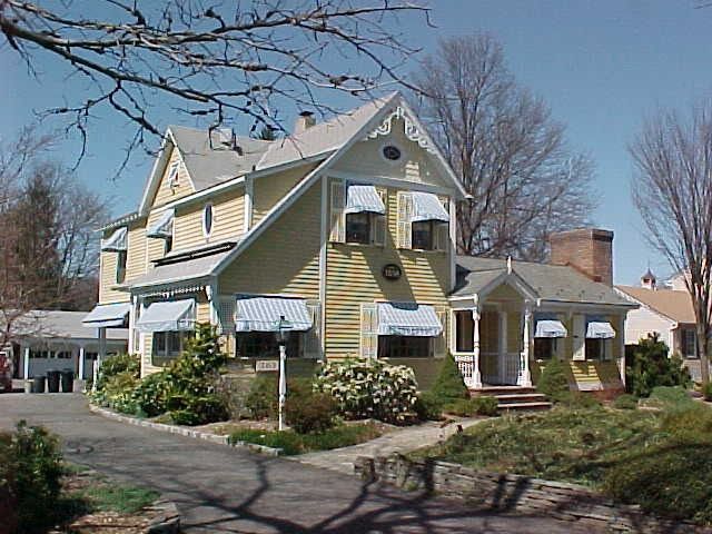 Yellow Victorian house with blue-striped awnings and a brick chimney on a sunny day.