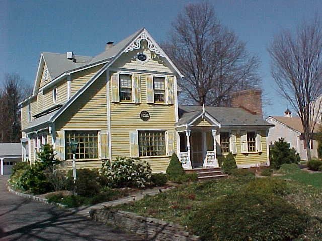 Yellow house with gray roof and trim, trees in front.