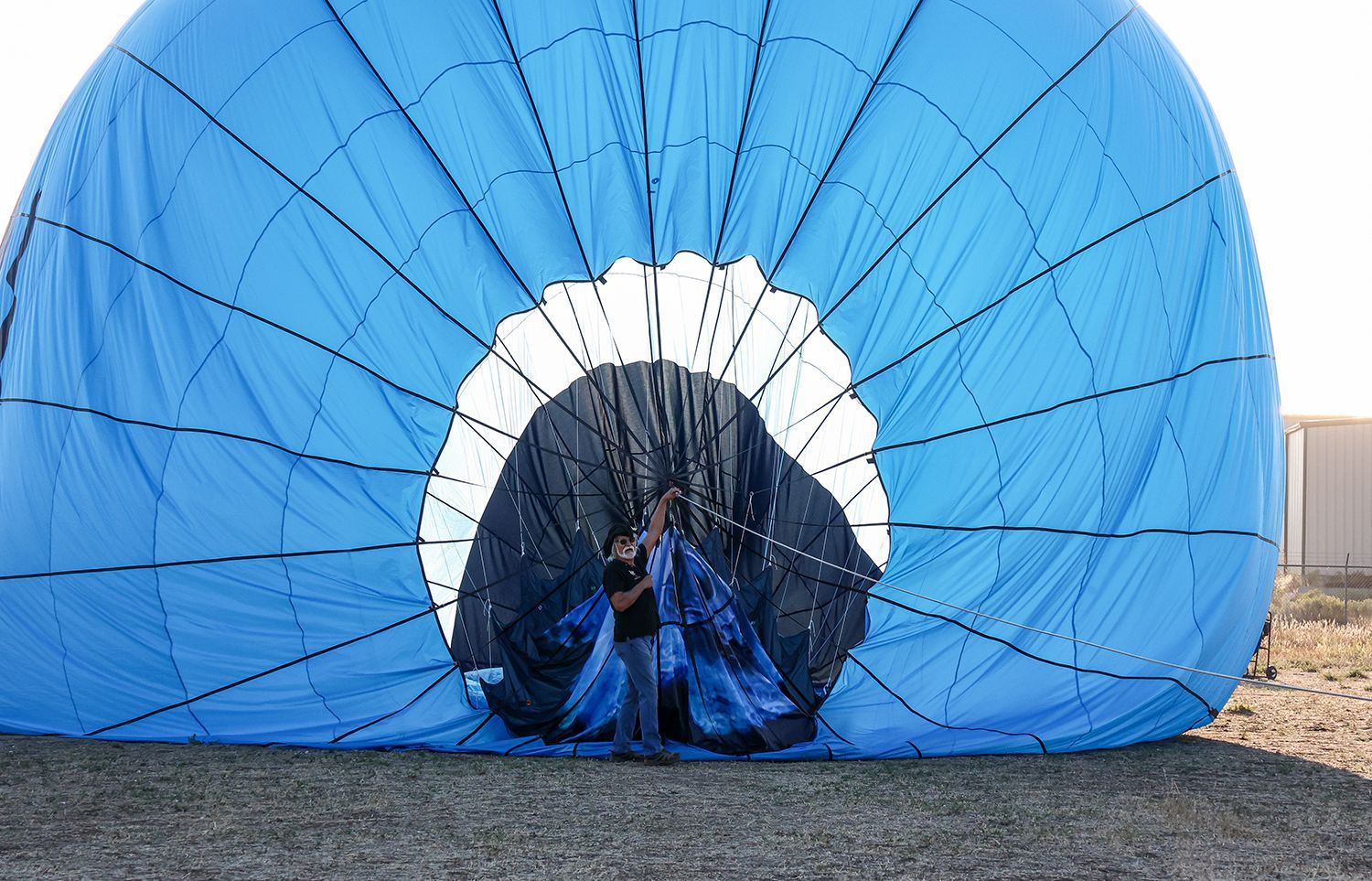 A person inside an inflating blue and black hot air balloon in a field.