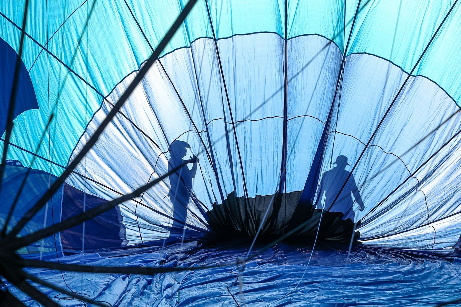 Inside a hot air balloon: Two silhouetted figures prepare for flight, blue and white fabric, interior view.
