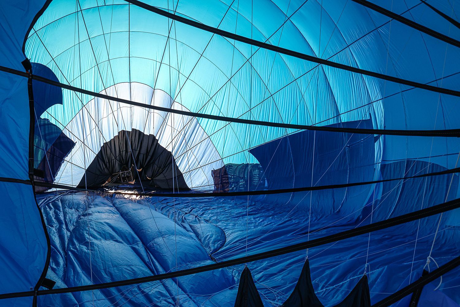 Inside a blue hot air balloon, lit by a bright opening; black rigging.