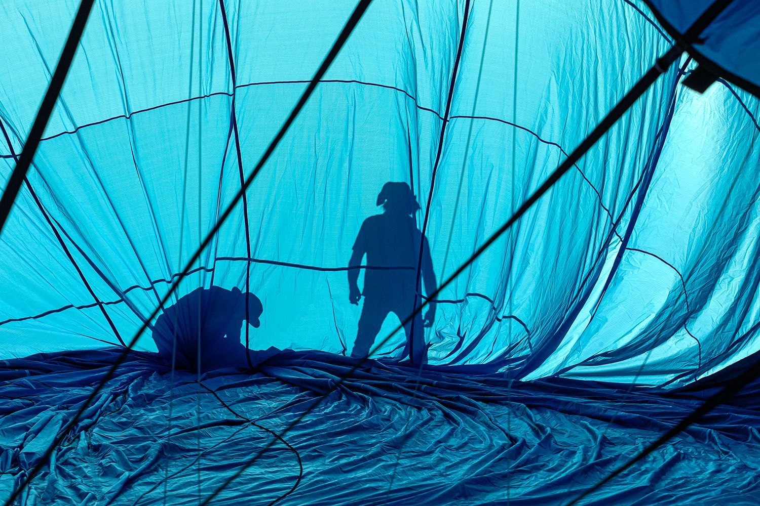 Silhouetted people inside a blue hot air balloon, preparing for flight.