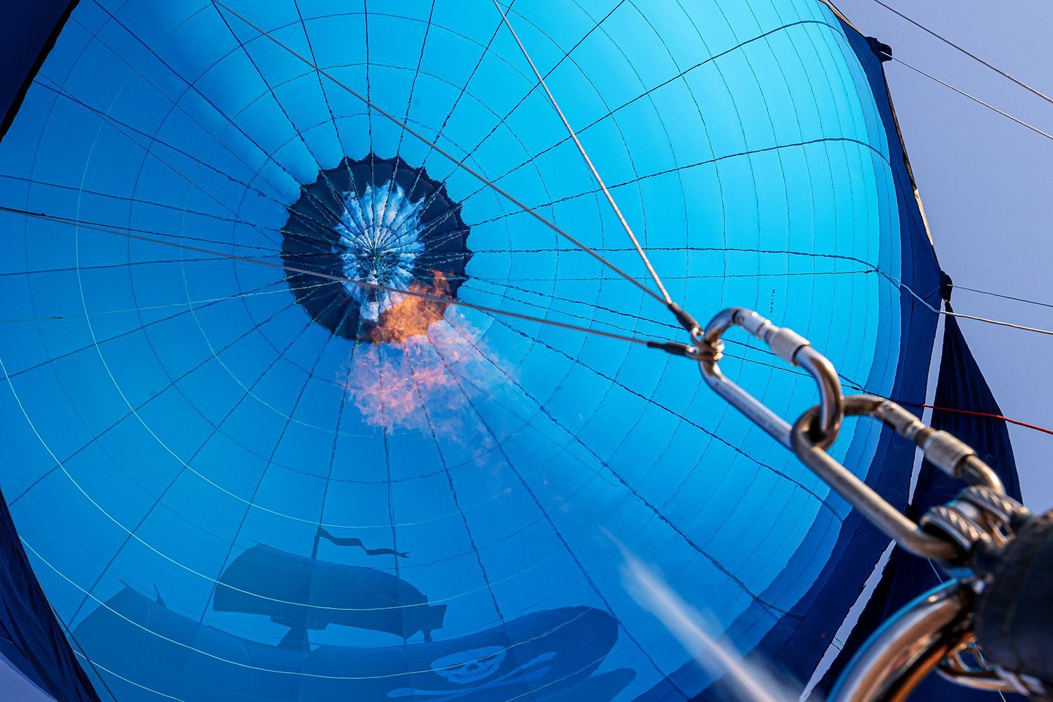 Blue hot air balloon interior with flames, silver carabiner, and basket silhouette.