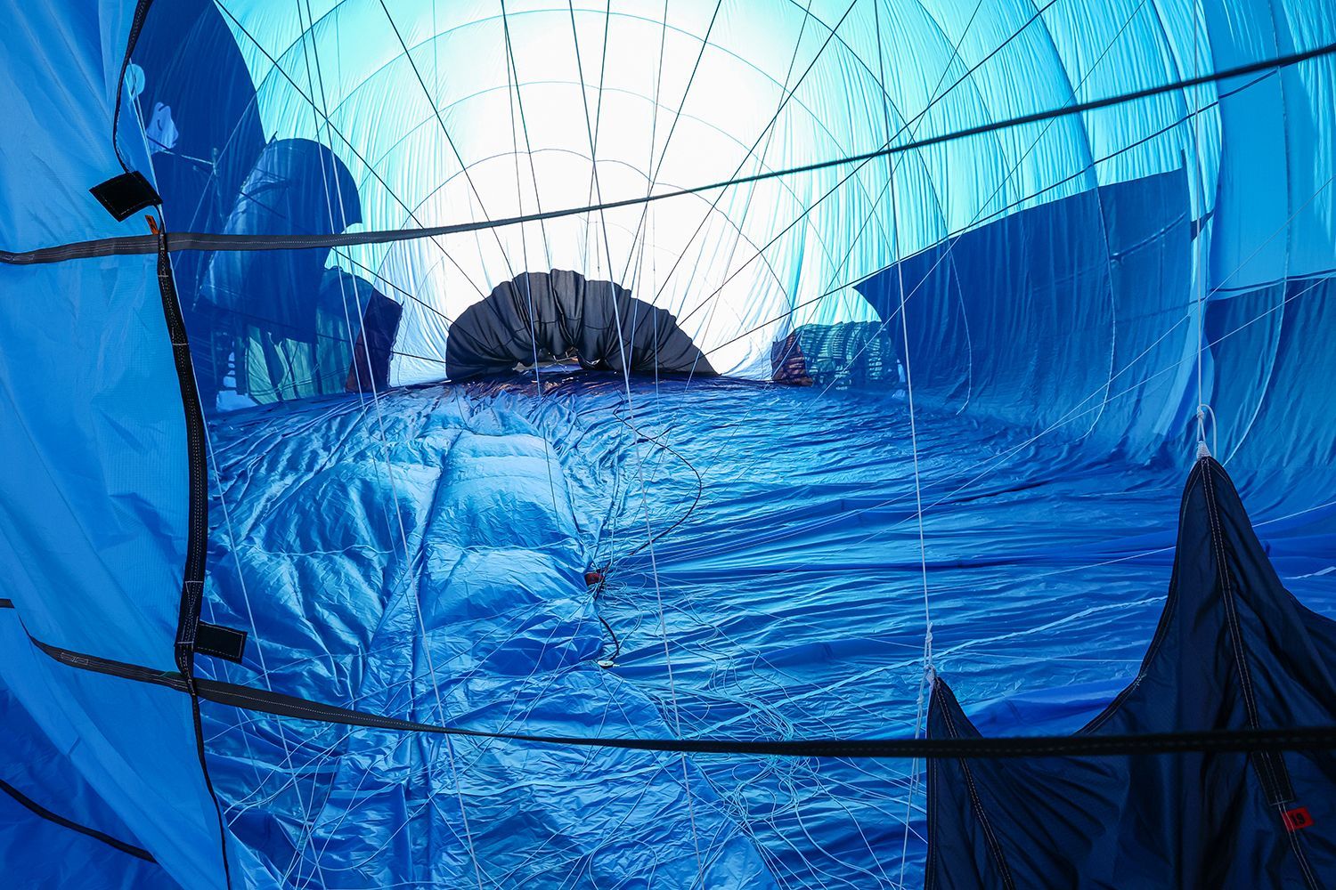 Inside view of a partially inflated blue hot air balloon. Sun shines through the opening at the top.