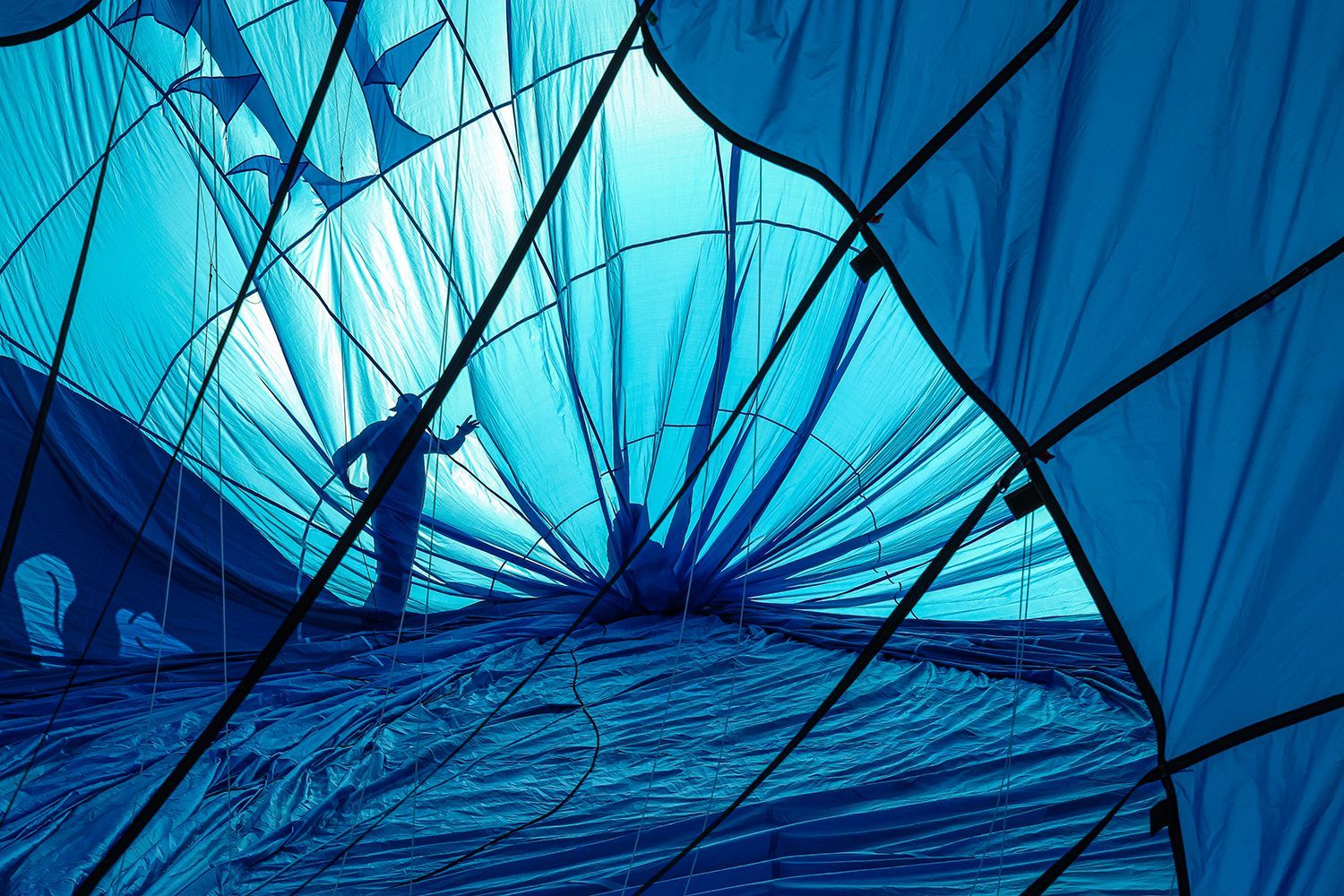Inside a blue hot air balloon, a silhouetted person prepares for flight.