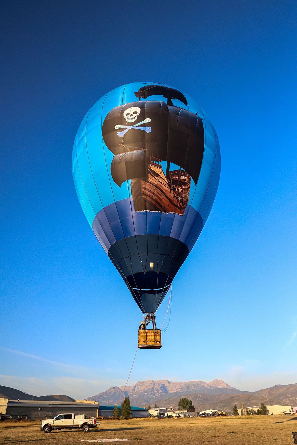 Hot air balloon with pirate ship illustration against a blue sky over a field.