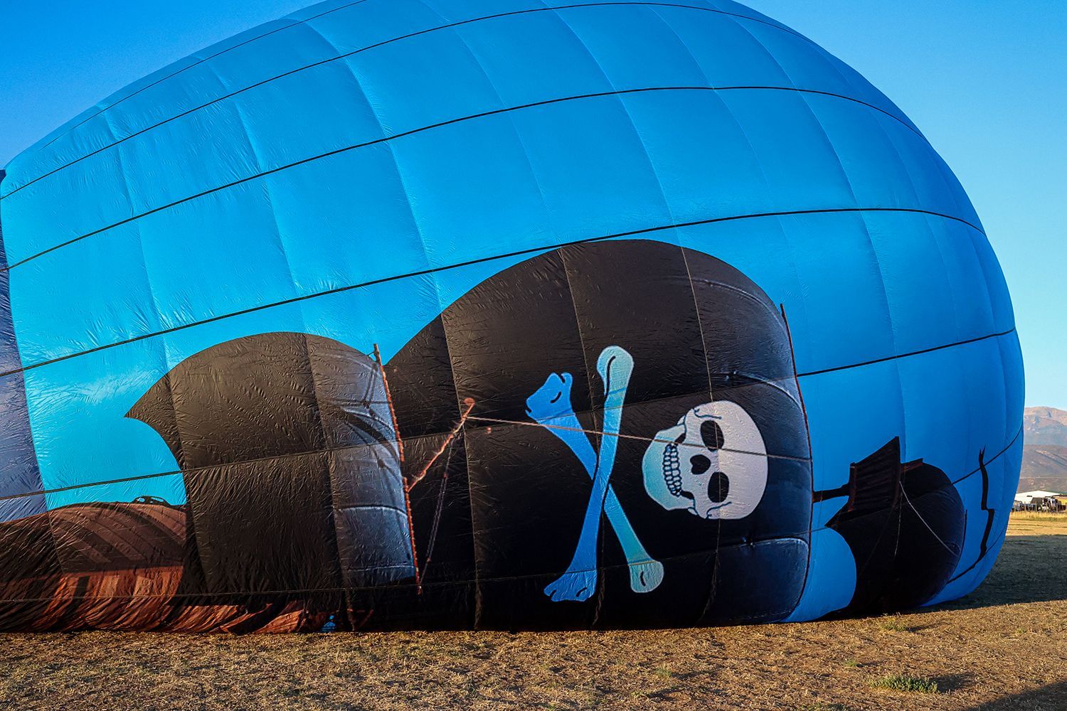 Blue and black pirate-themed hot air balloon lying on the ground with a skull and crossbones on the side.