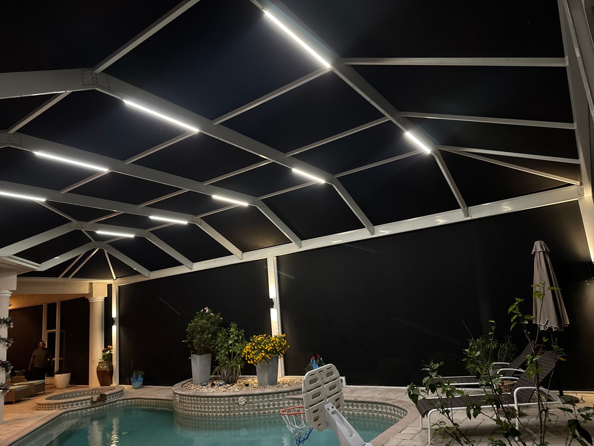 Pool enclosure with overhead LED lights illuminating the dark screen and a pool below.