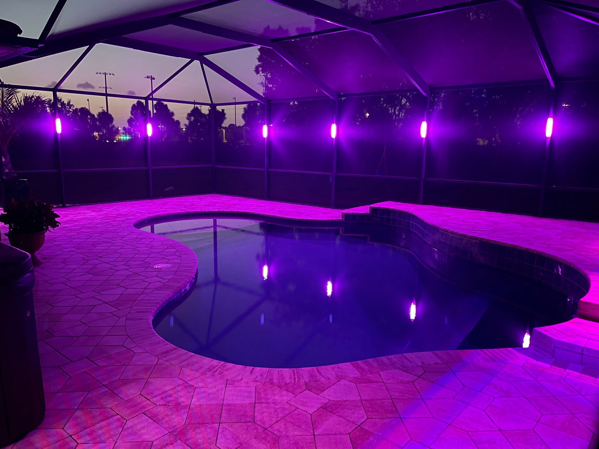 Purple-lit pool under a canopy at night, with tiled deck and reflections in the water