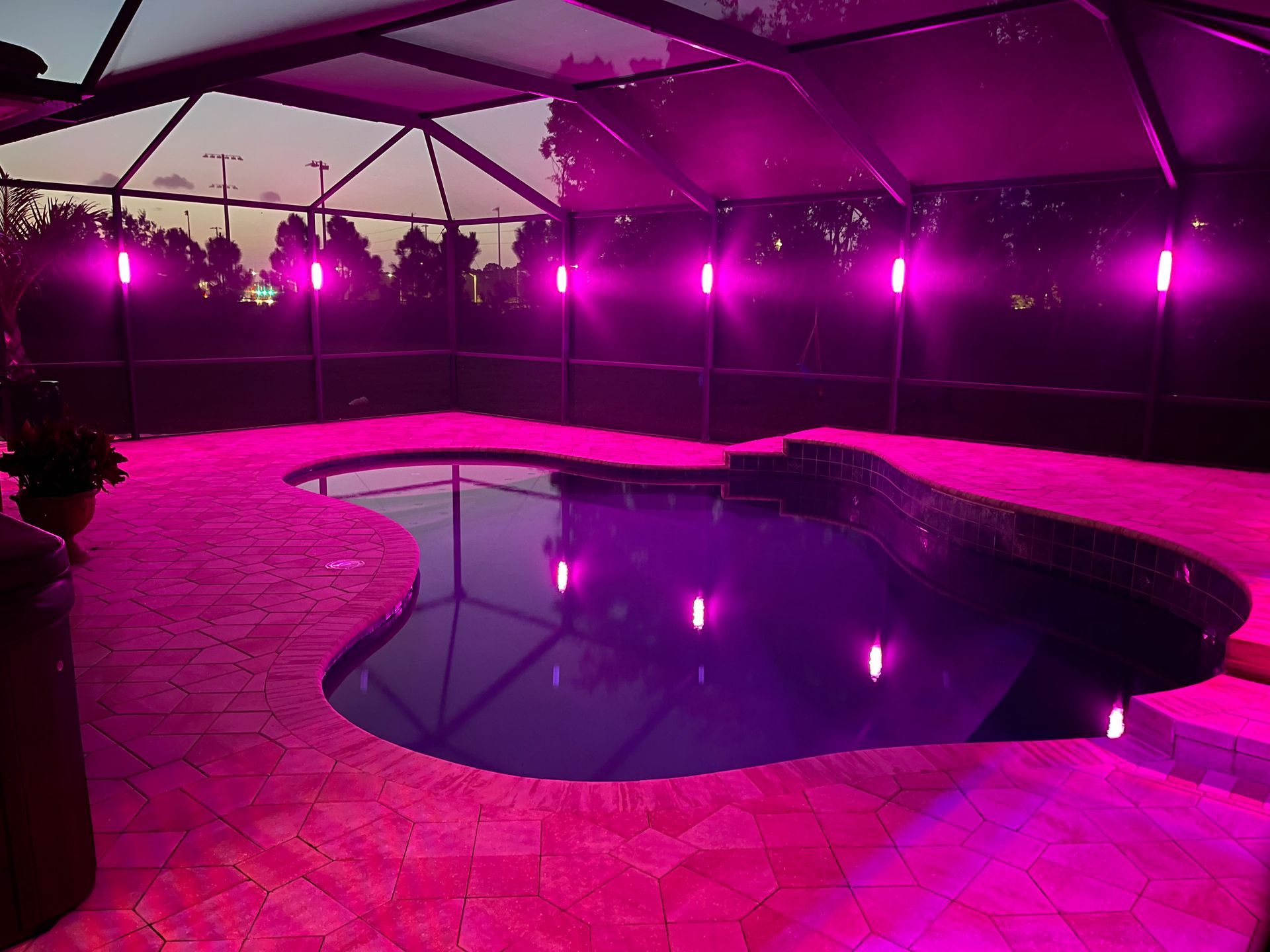 Indoor pool under magenta lighting with a curved stone deck and reflective water