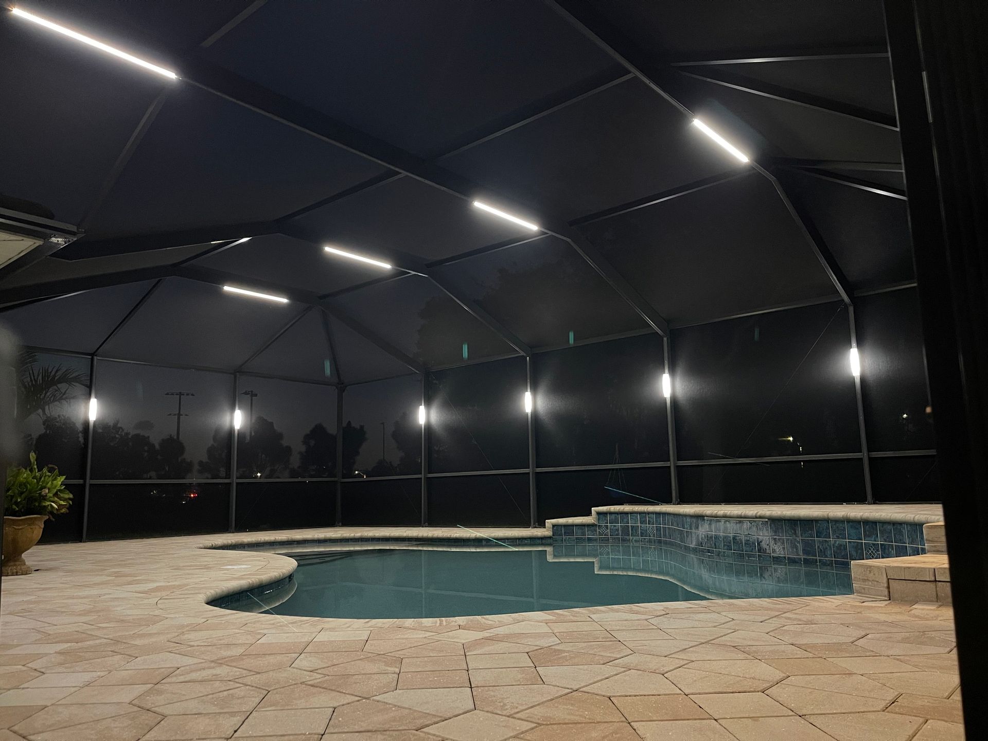 Screened-in pool patio at night with lit pool, stone deck, and dark canopy overhead