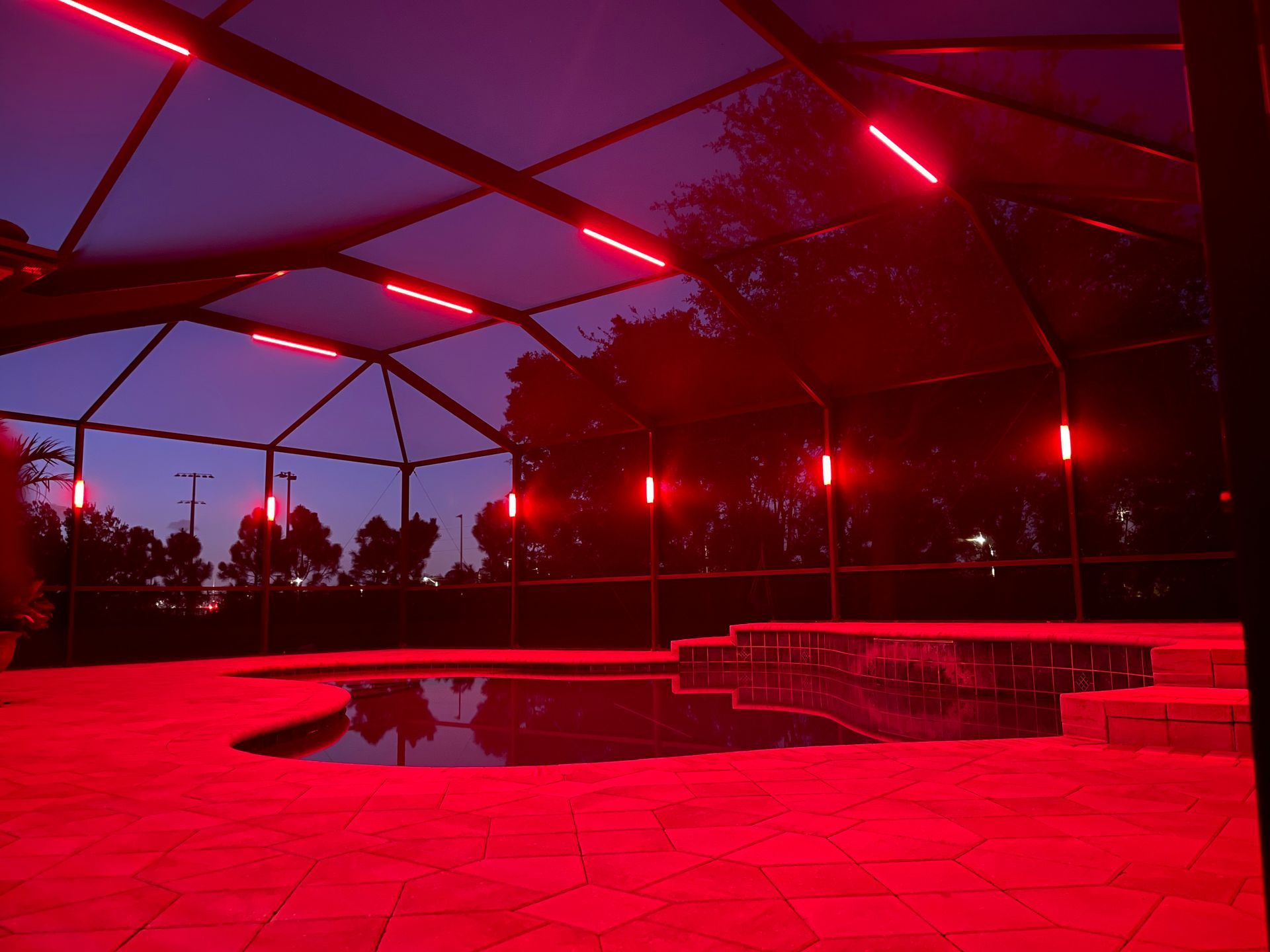 Red-lit poolside patio under a screened canopy at dusk