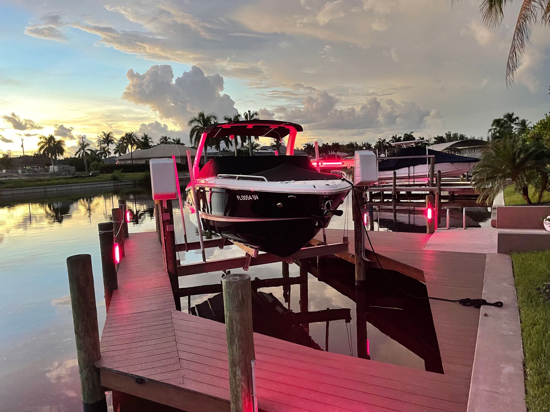 Boat docked on a lift with red lights, reflecting in the water at sunset.