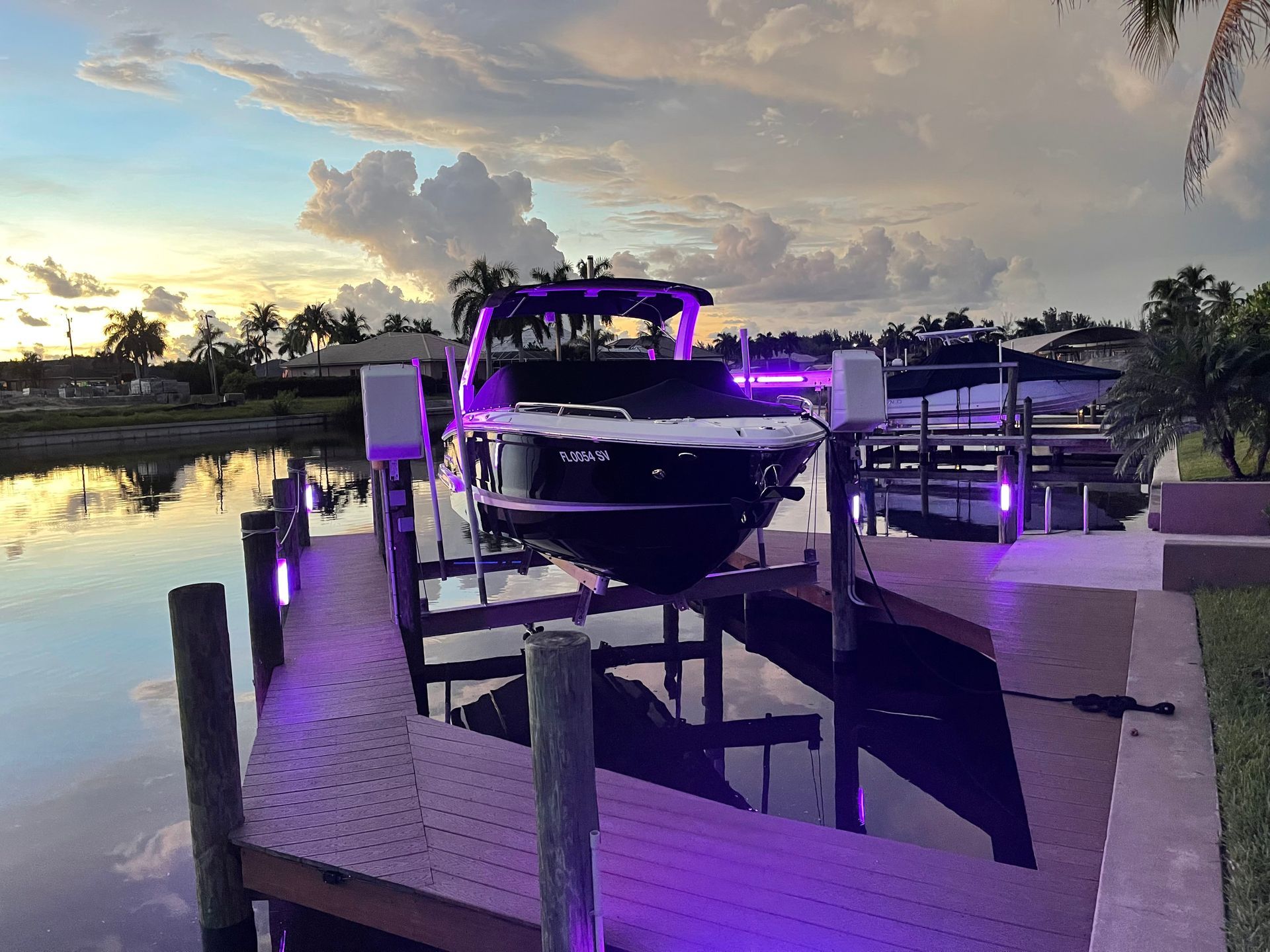 Boat on a lift at sunset, illuminated by purple lights. Water and a cloudy sky are in the background.