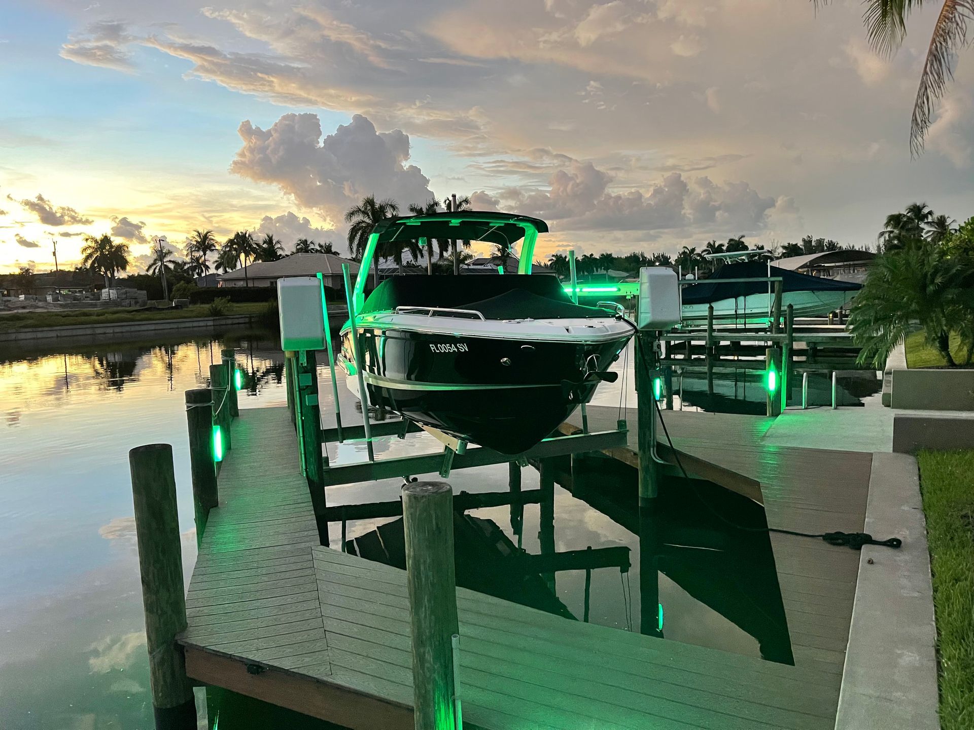 Boat on a lift in a canal at sunset with green lights illuminating the dock.