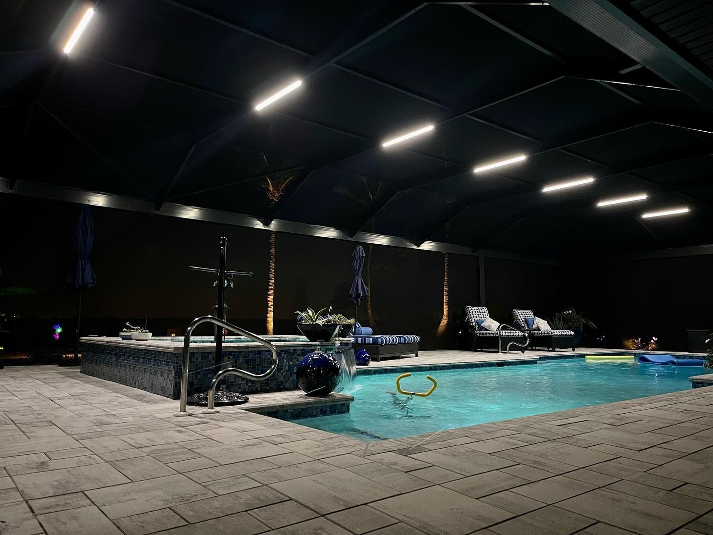 Pool illuminated at night under a covered patio with lounge chairs.