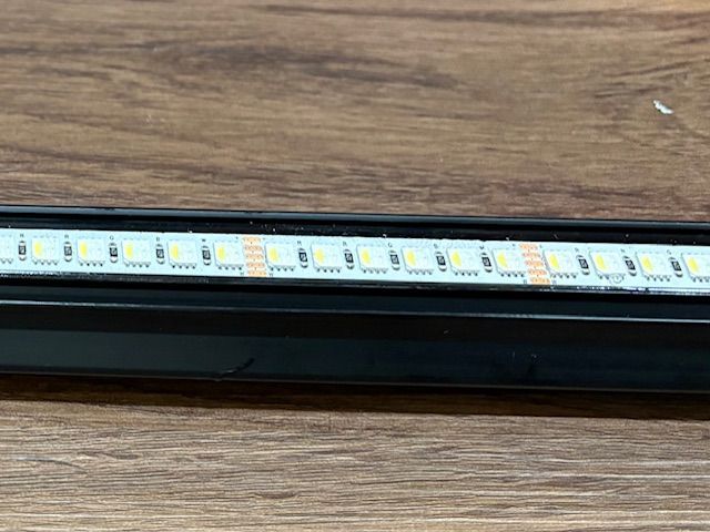 Black LED light strip with white and yellow LEDs on a wooden surface.