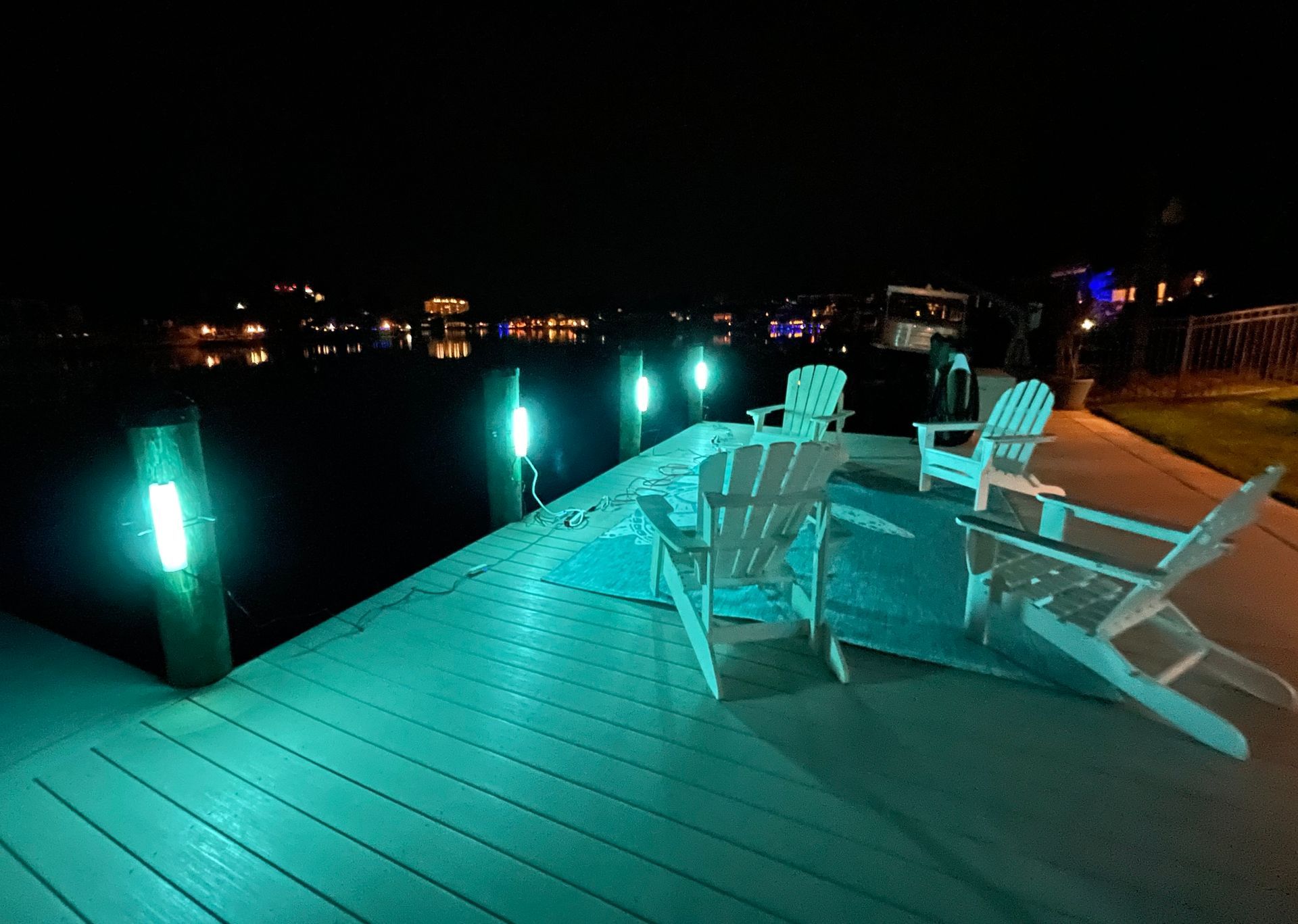Night dock with white lounge chairs lit by turquoise lights beside dark water