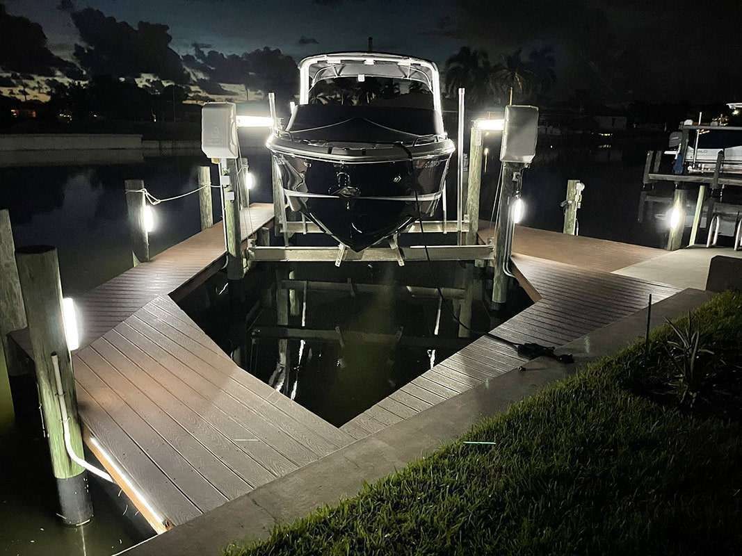 Lit boat on a reflective dock display at night, surrounded by water and walkway lights.