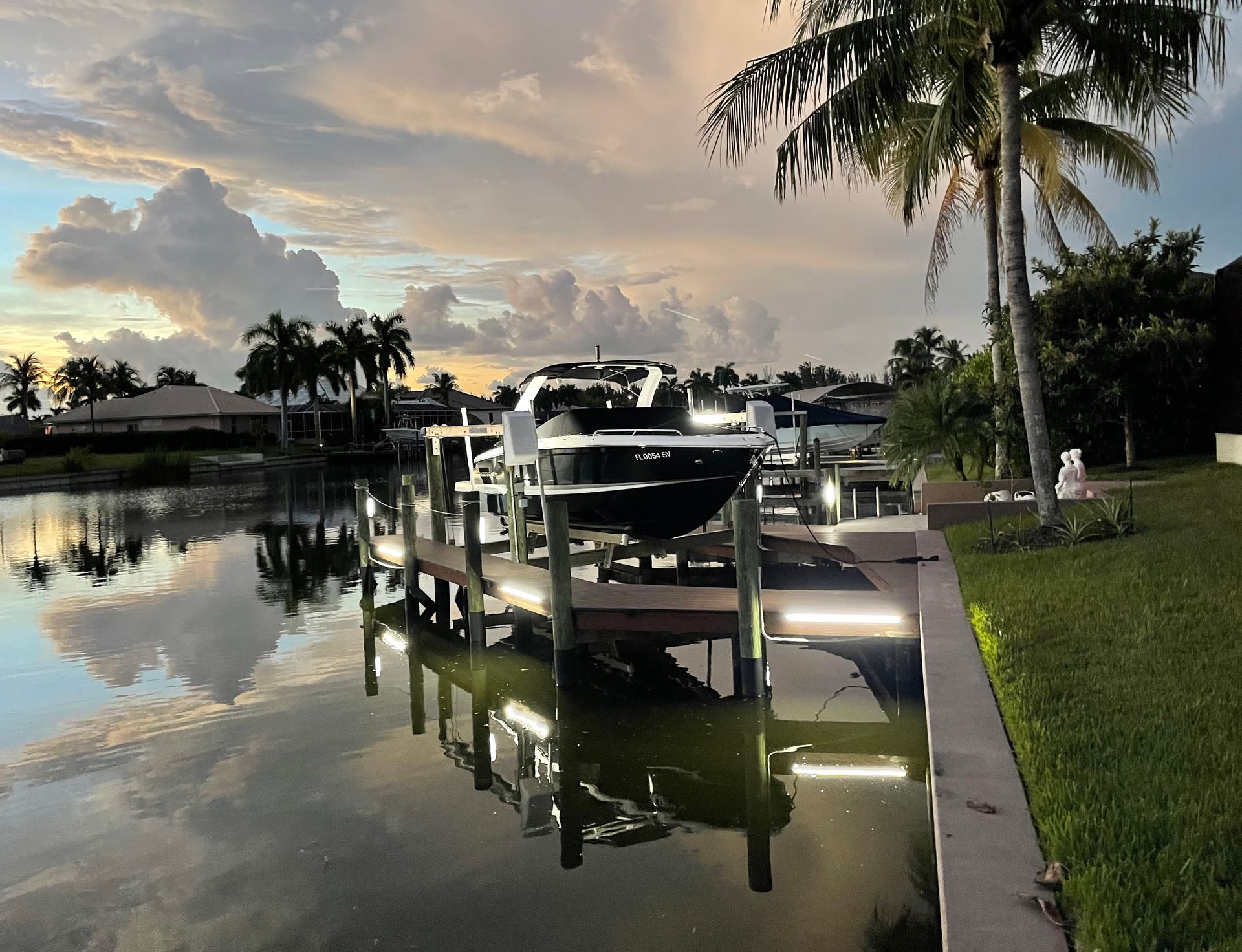 Boat docked on a calm canal at sunset, with palm trees and reflections in the water.