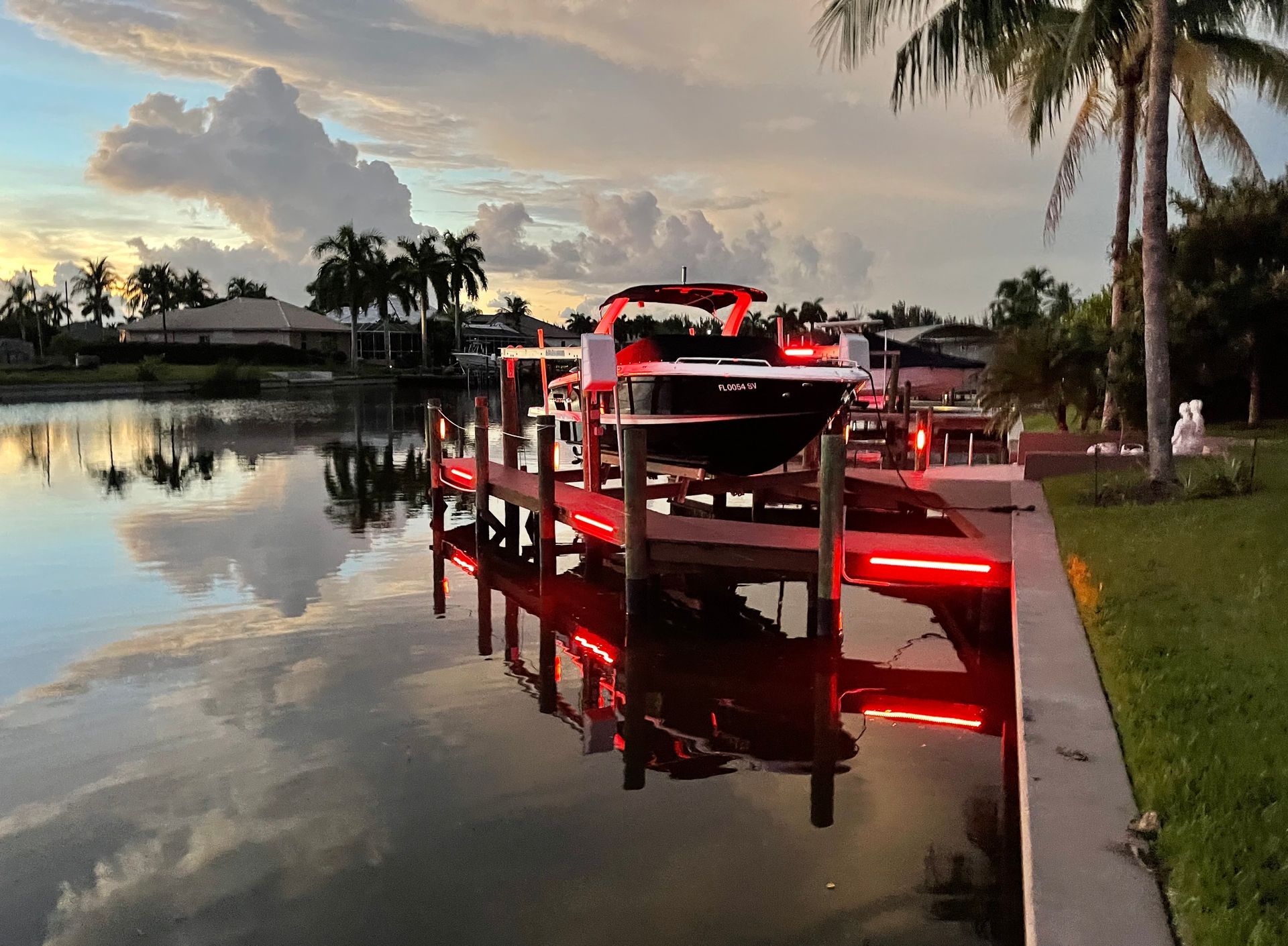 Red-lit boat dock on a calm canal at sunset with a jet ski and palm trees reflected in the water