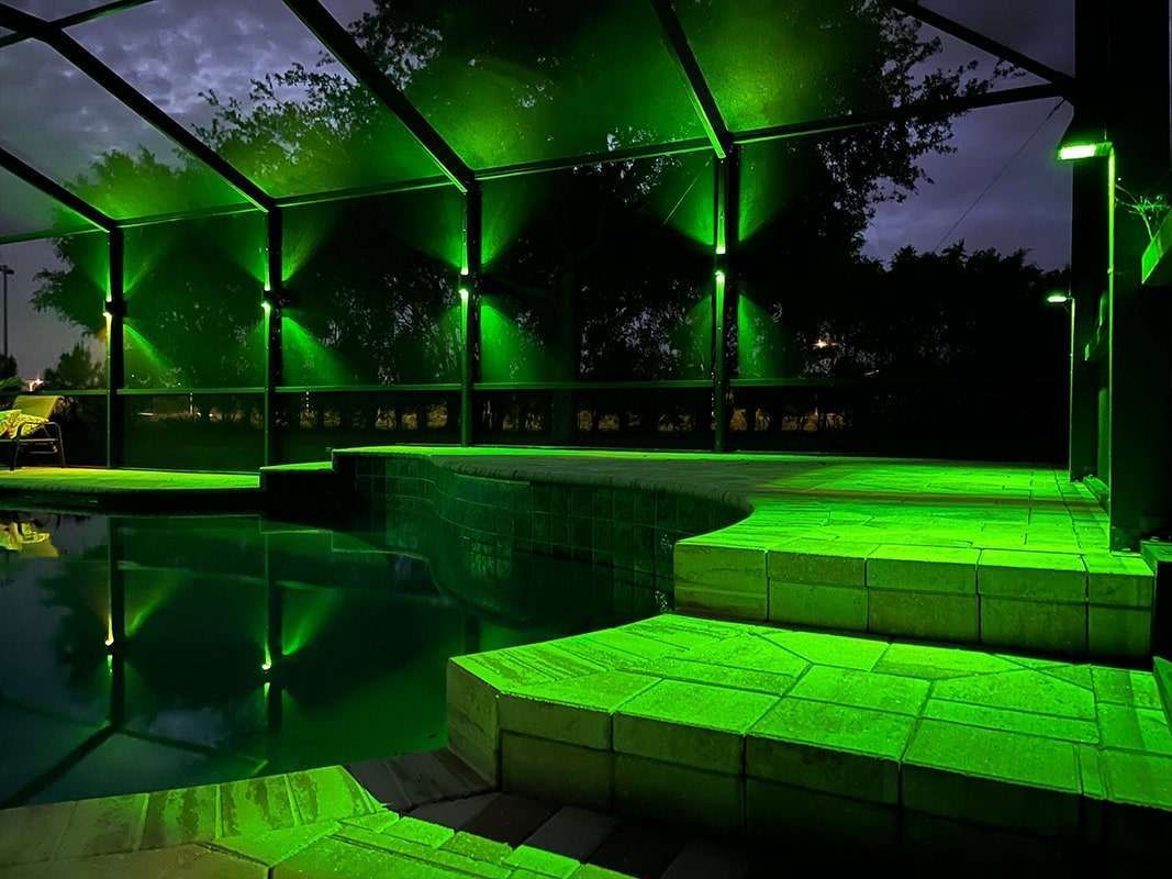 Green-lit outdoor pool beside steps and a covered patio at night