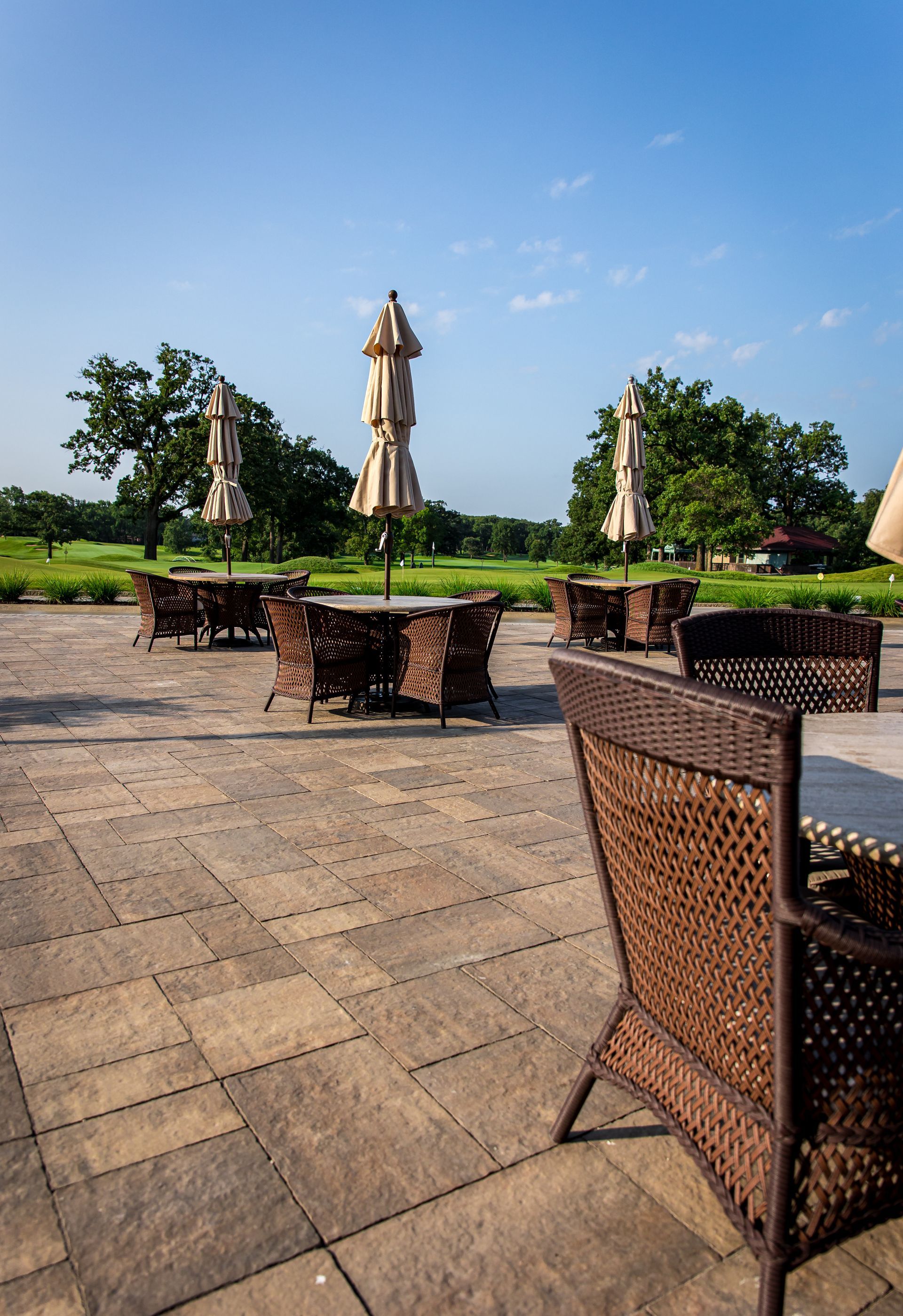 A patio with wicker chairs , tables and umbrellas on a sunny day.