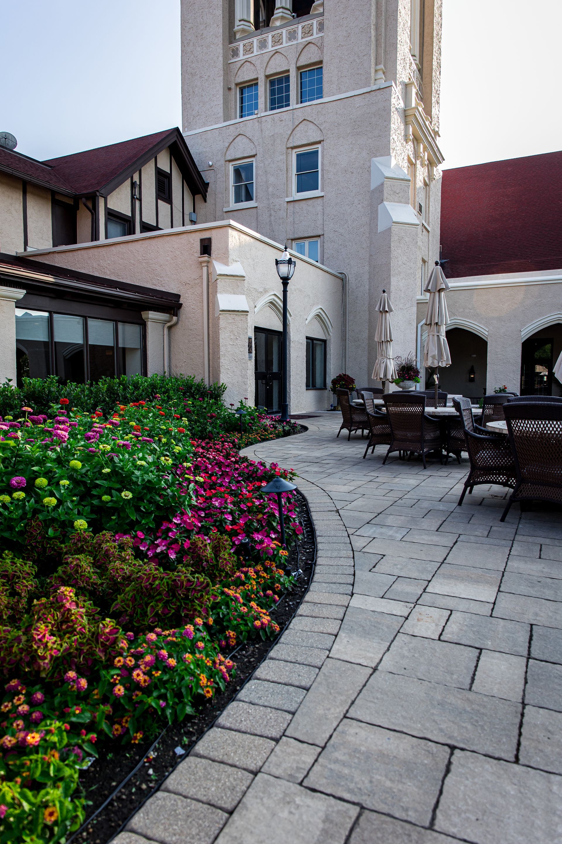A patio with tables and chairs and flowers in front of a large building.