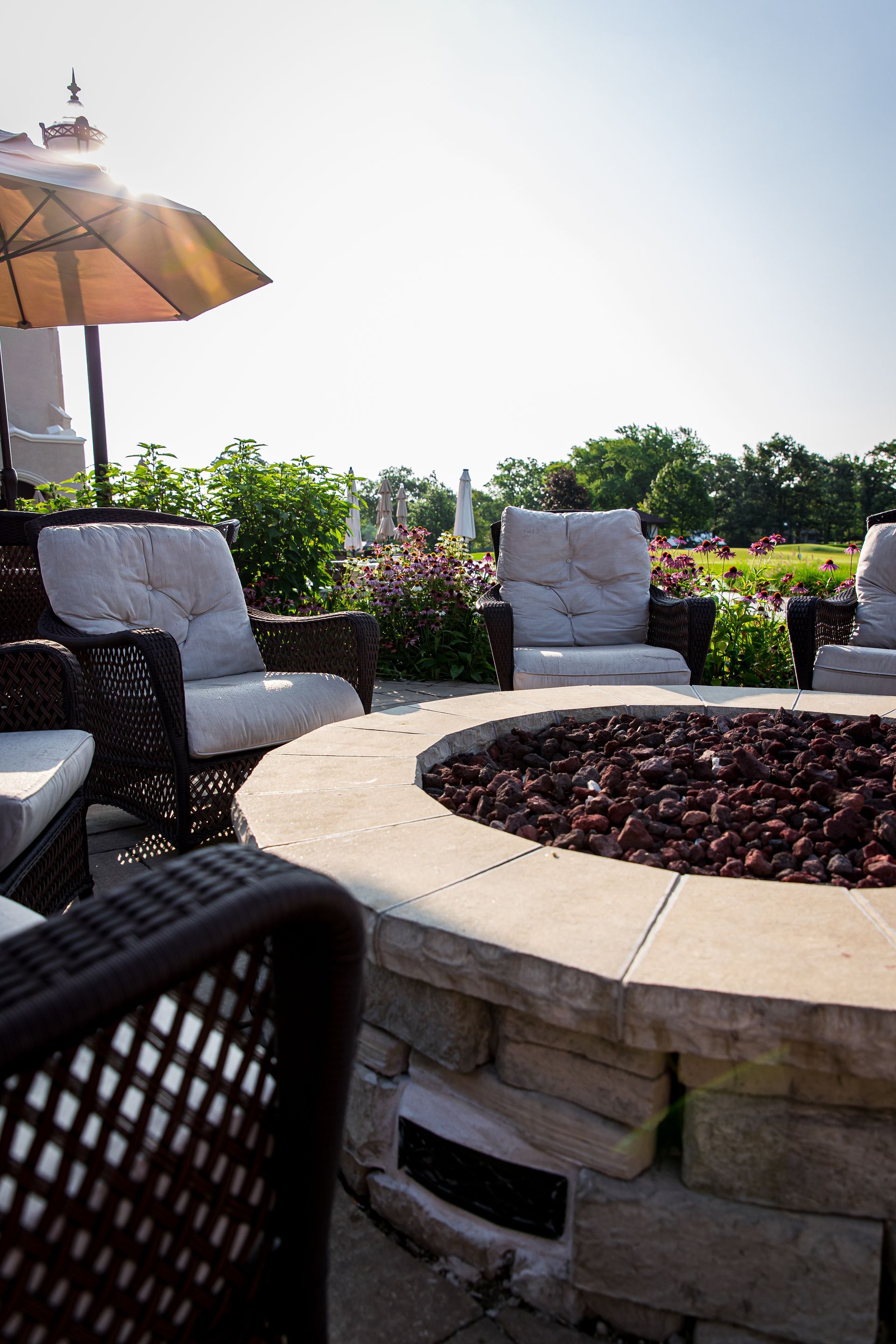 A fire pit surrounded by chairs and umbrellas on a patio.