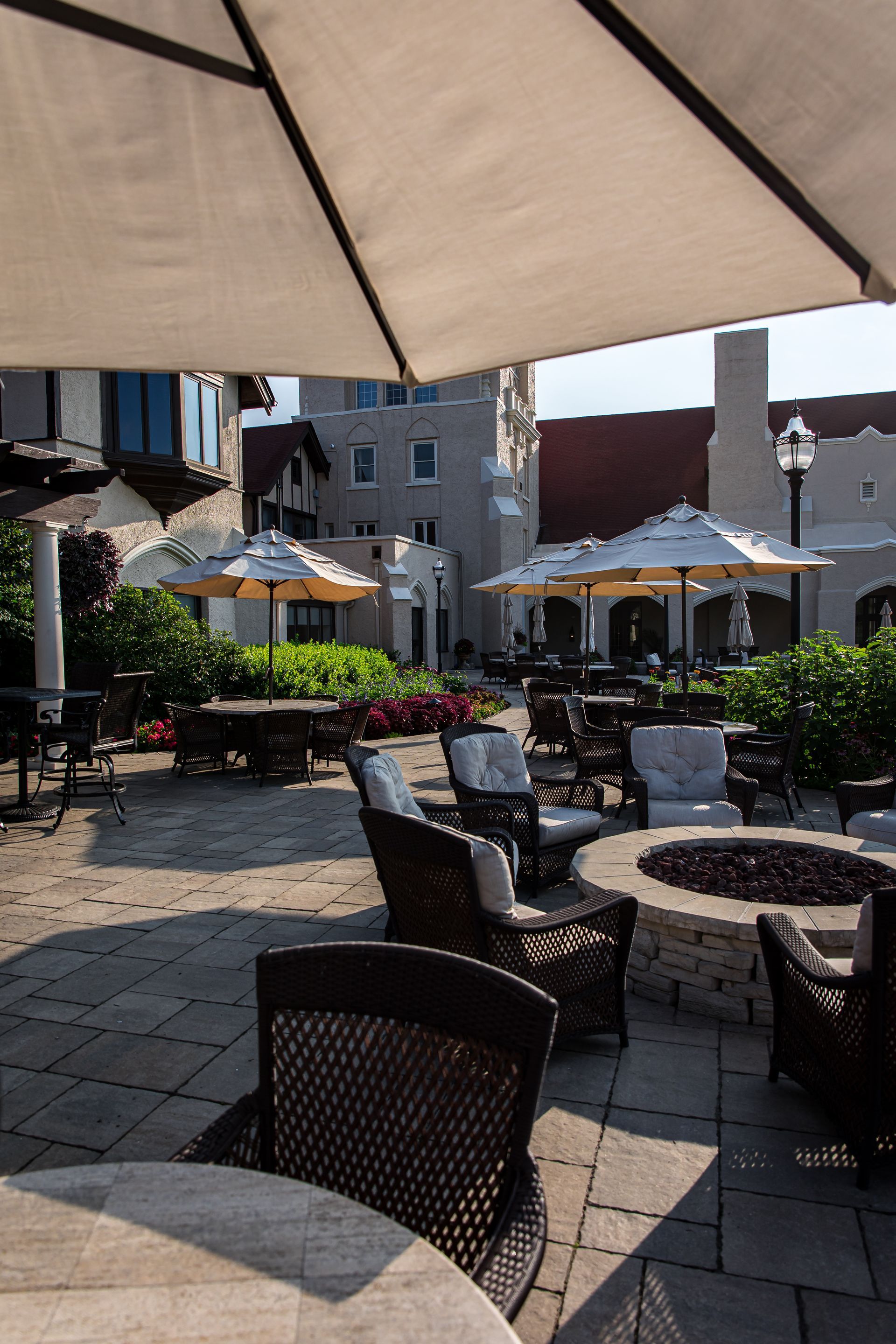 A patio with tables , chairs , umbrellas and a fire pit.