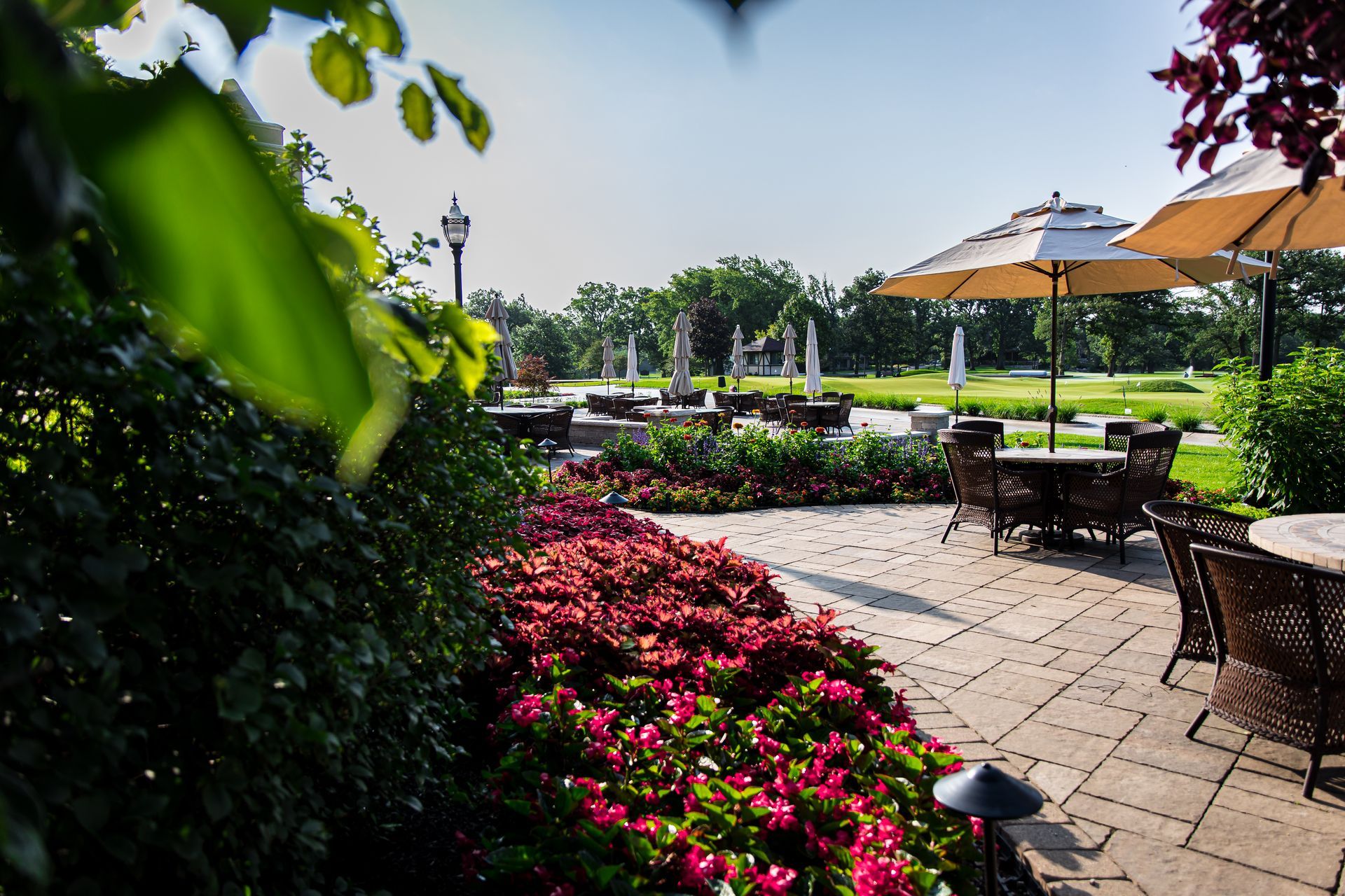 A patio with tables and chairs and umbrellas surrounded by flowers.