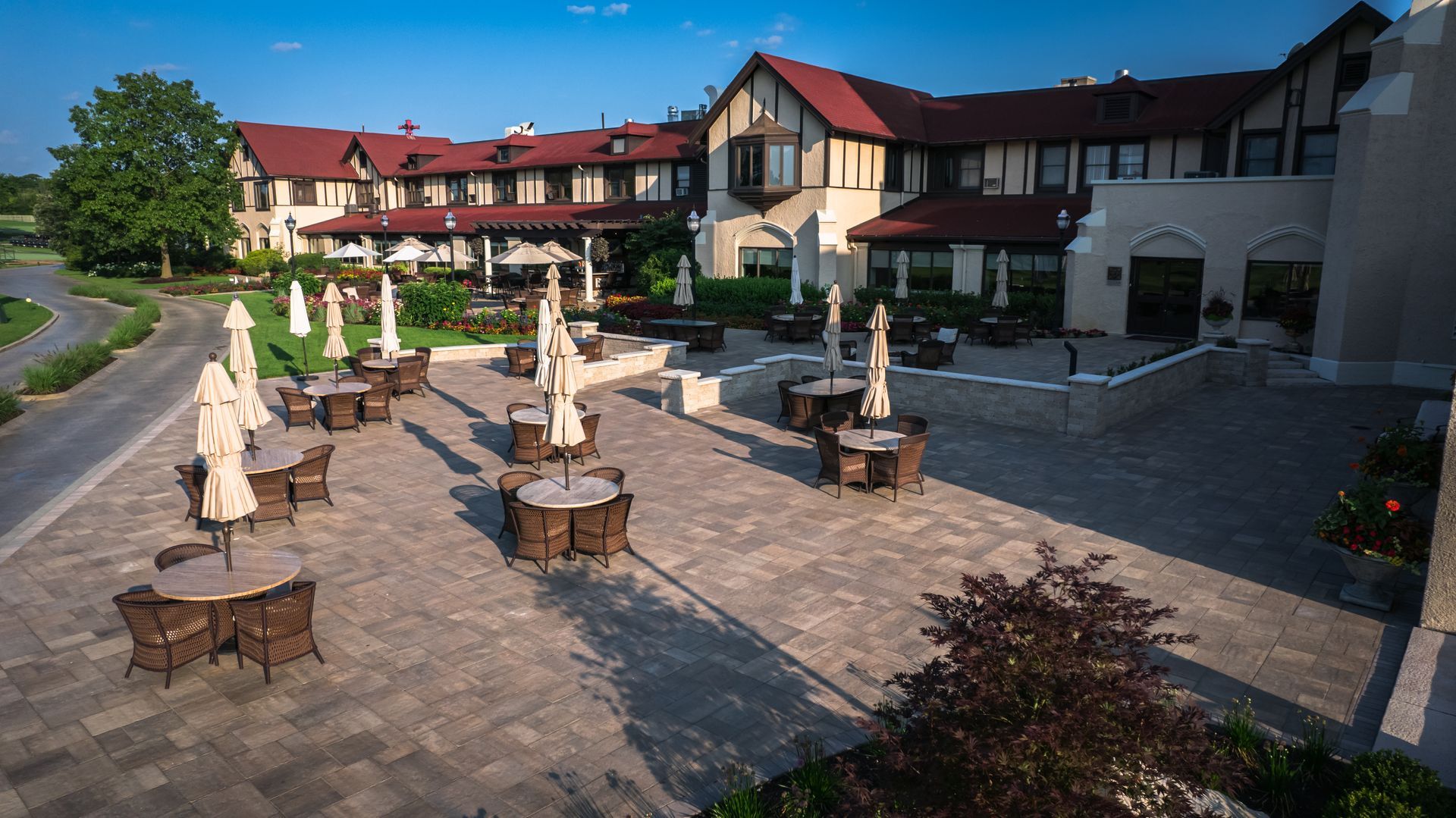 An aerial view of a large building with tables and chairs and umbrellas in front of it.