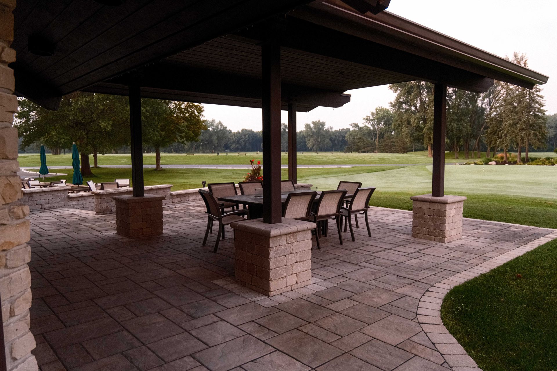 A patio with tables and chairs under a canopy overlooking a golf course