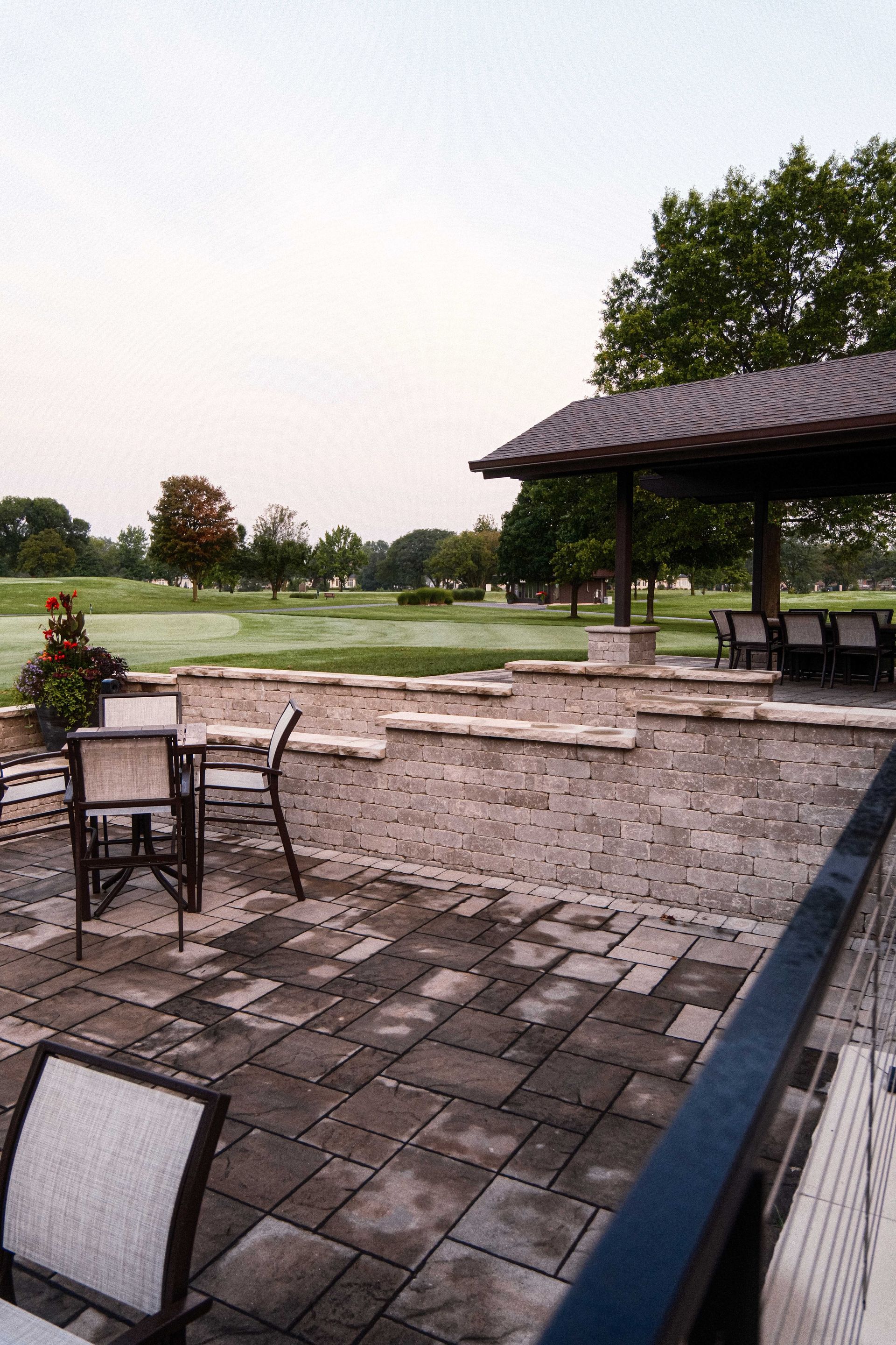 A patio with tables and chairs and a gazebo overlooking a golf course.