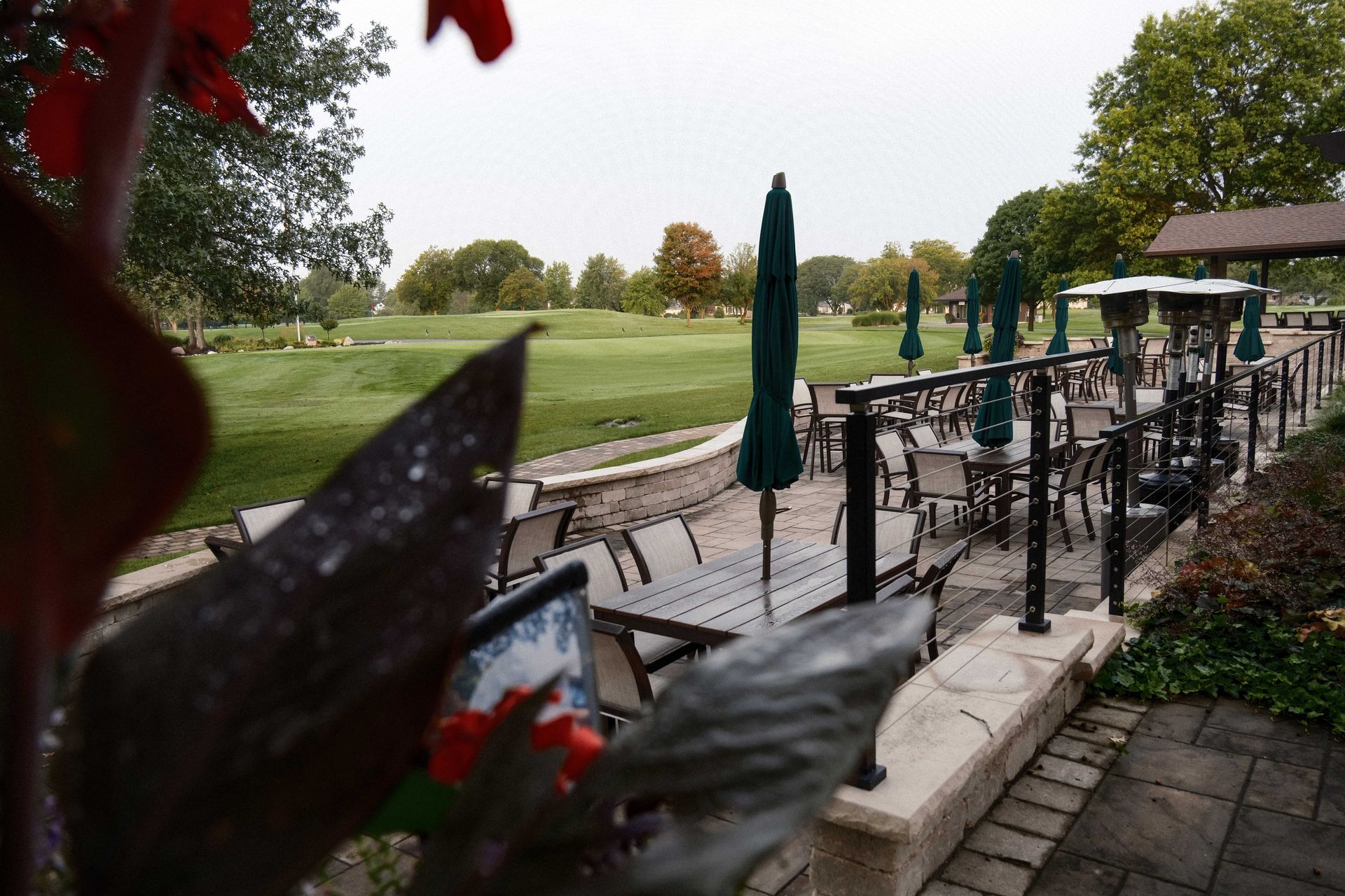 A patio with tables and chairs and umbrellas in front of a golf course.