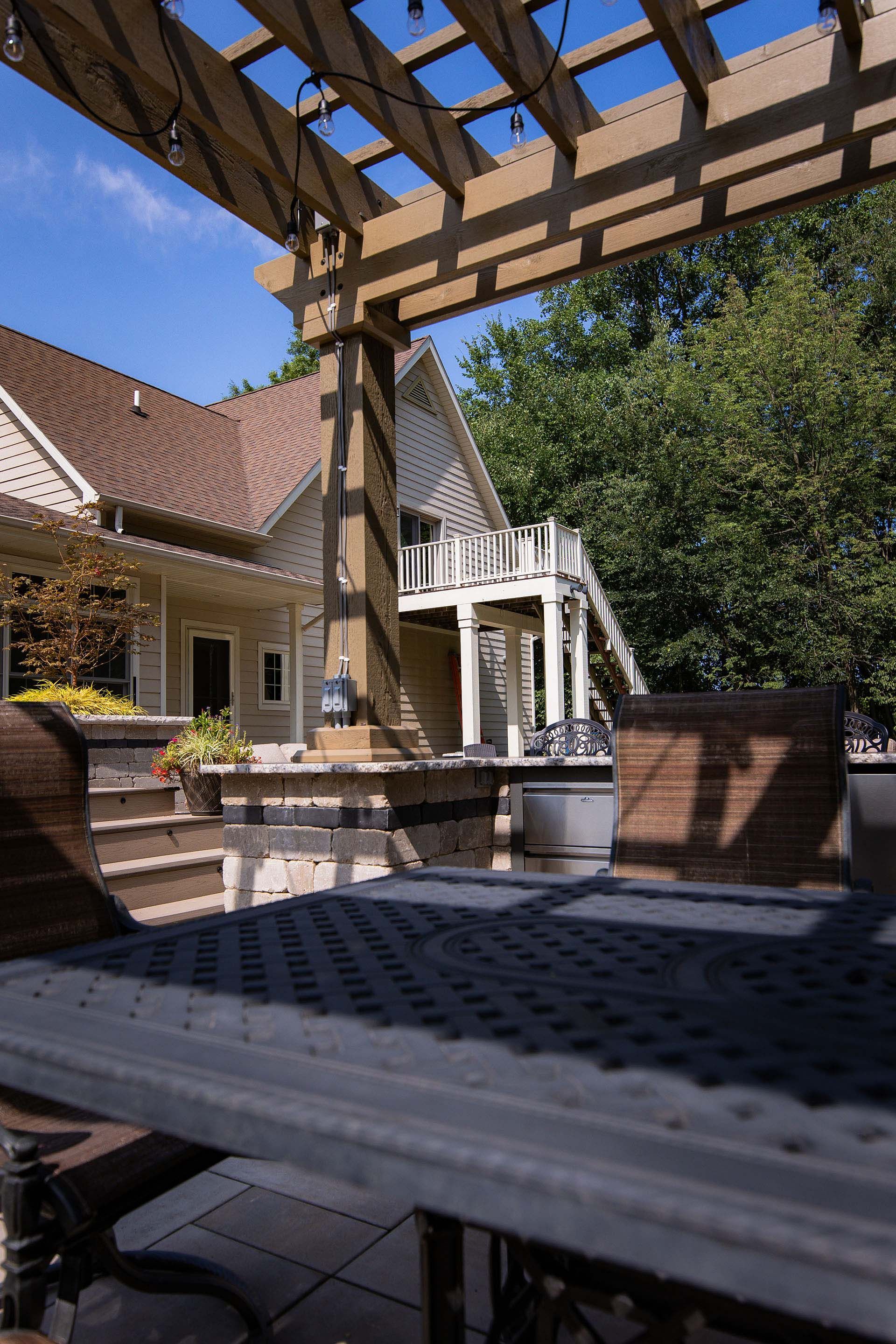 A table and chairs under a pergola in front of a house.