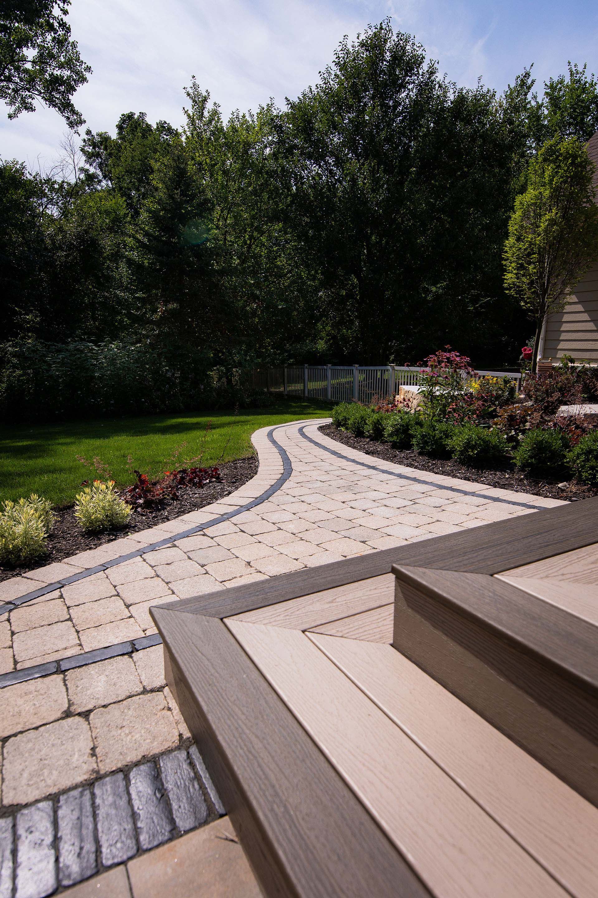 A patio with a brick walkway leading to a lush green yard.