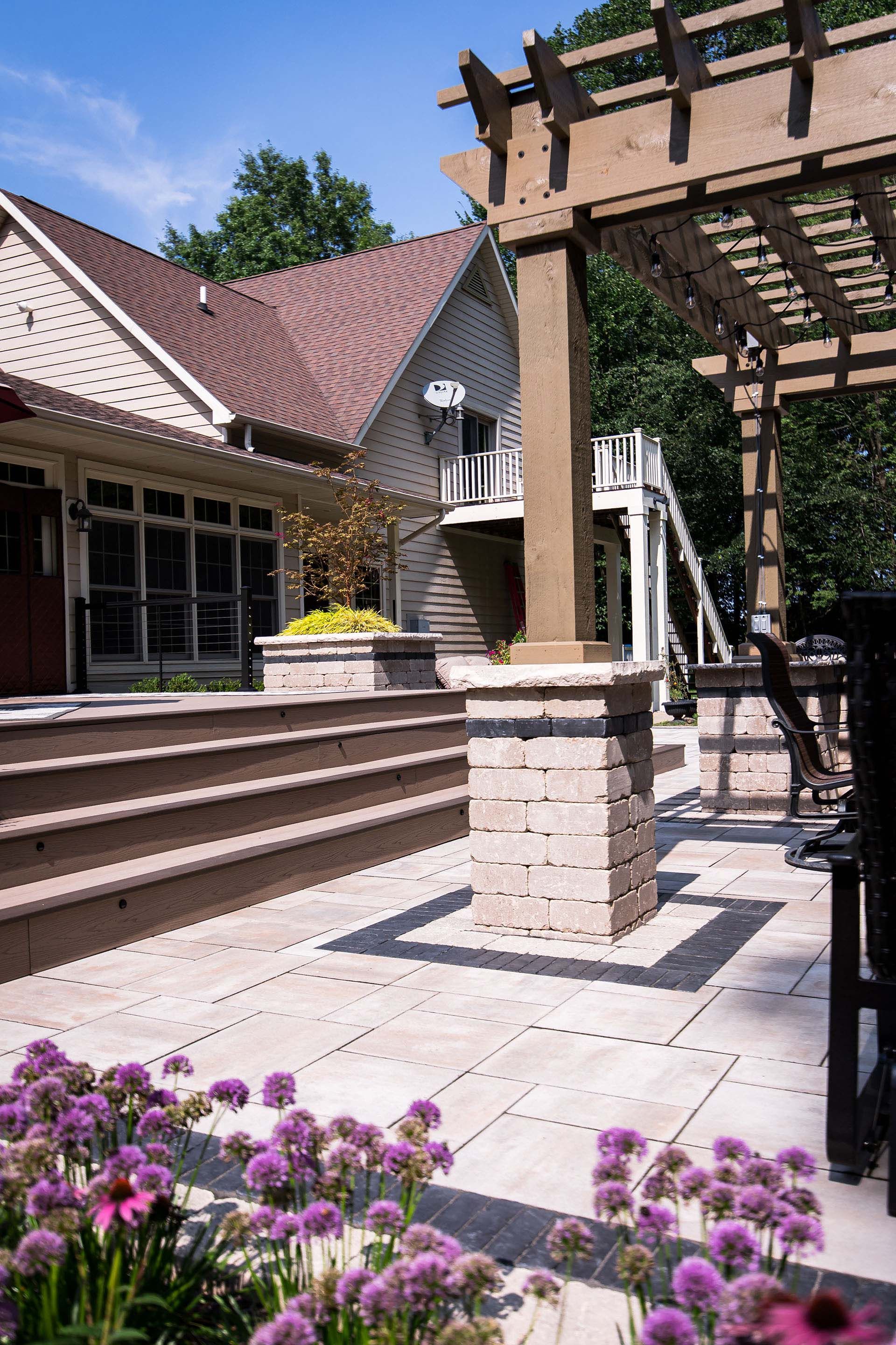 A patio with a pergola and purple flowers in front of a house.