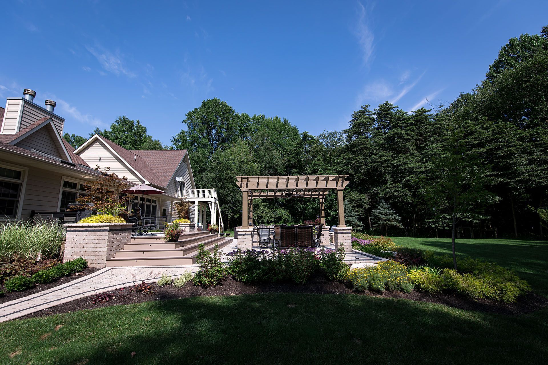 A large house with a pergola in the backyard surrounded by trees.