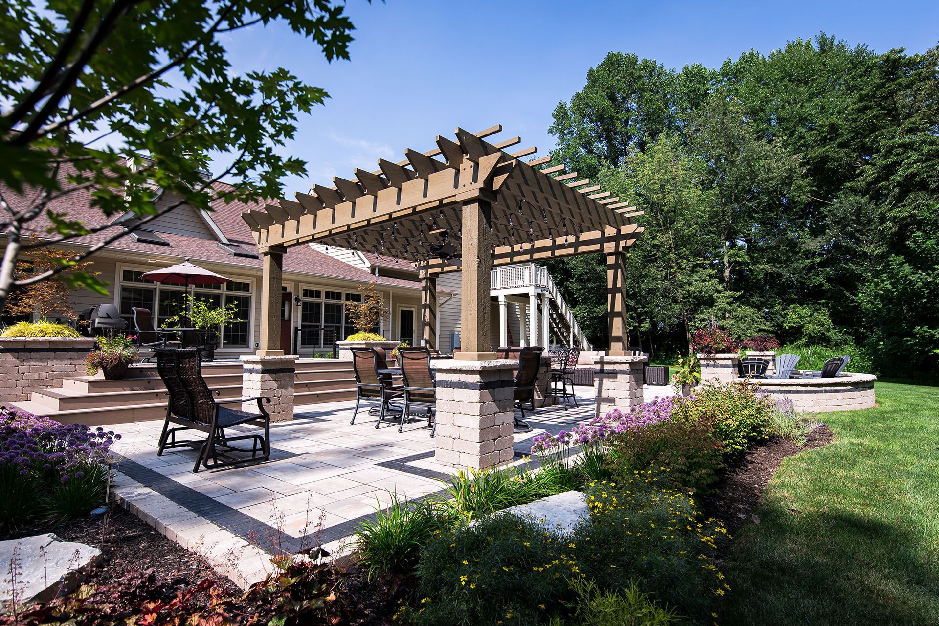 A large patio with a pergola and chairs in front of a house.