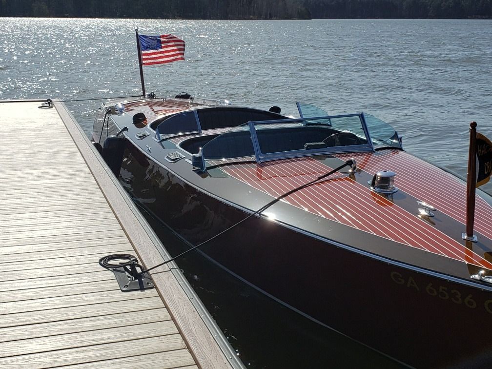 Wooden speedboat docked, American flag waving, sunny day on the water.
