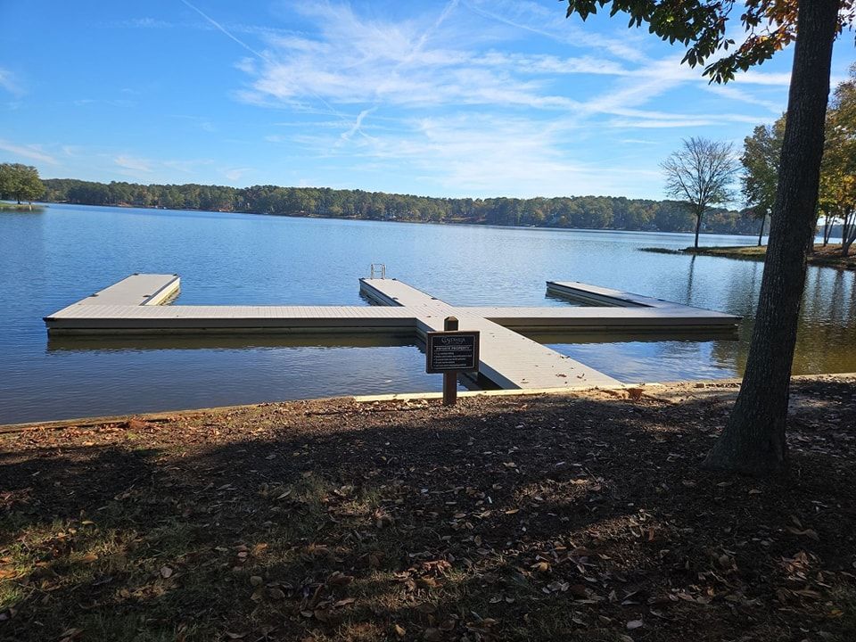 Dock extending into a lake, with a sign in front; blue sky and trees in background.