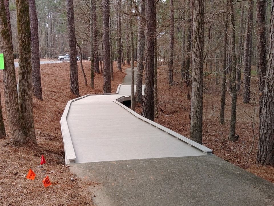 Boardwalk path winding through a forest of tall trees, with orange cones along the side.