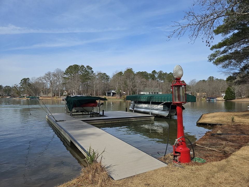 Dock on a lake with covered boats, a vintage red gas pump, and trees under a blue sky.