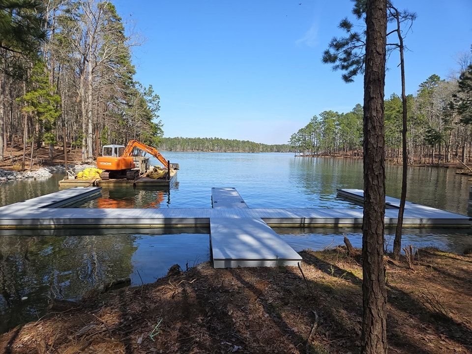 A lake with docks and an excavator. Trees surround the water under a blue sky.