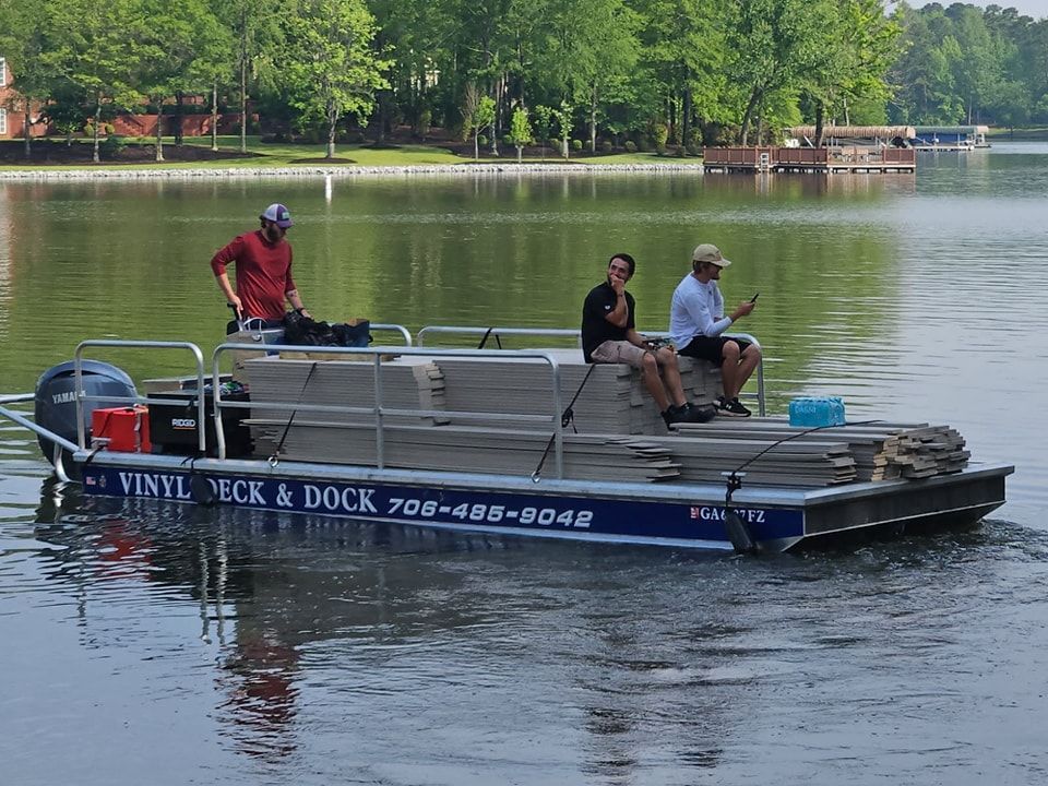 A boat with stacked lumber and three people on board travels on a lake. The boat is labeled 