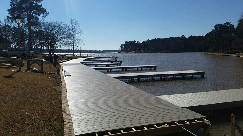 Docks extending into a brown lake under a blue sky, with trees on the far shore and grassy area in the foreground.
