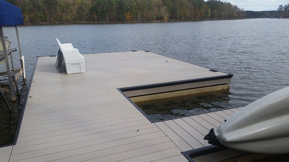Dock extending into lake, light tan surface, white bench, water, trees in the background.