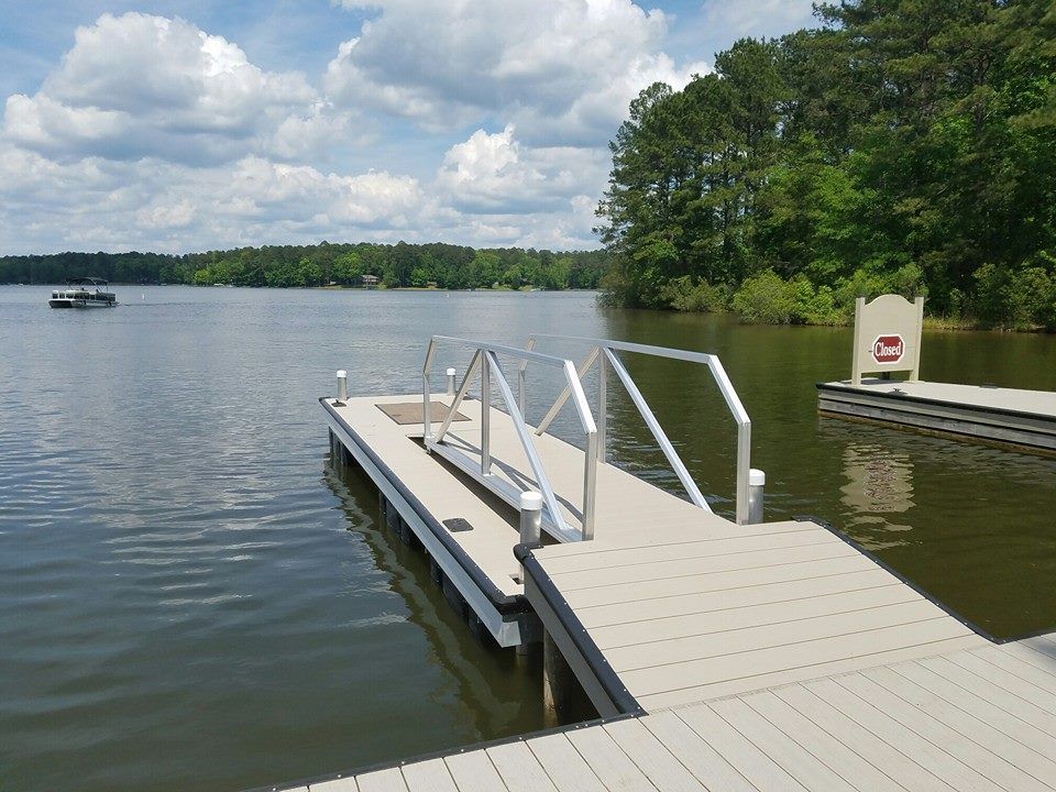 Dock extending into a lake, with a ramp and handrails. Trees and cloudy sky in background.