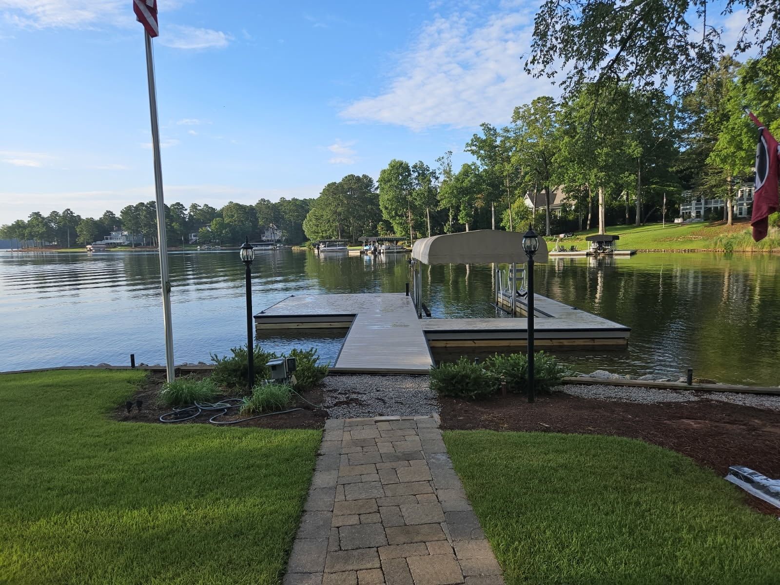 Path leads to dock on lake under a sunny sky with trees lining the shore.